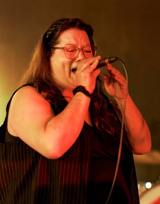 Patty Waltrip singing into a microphone under red stage light